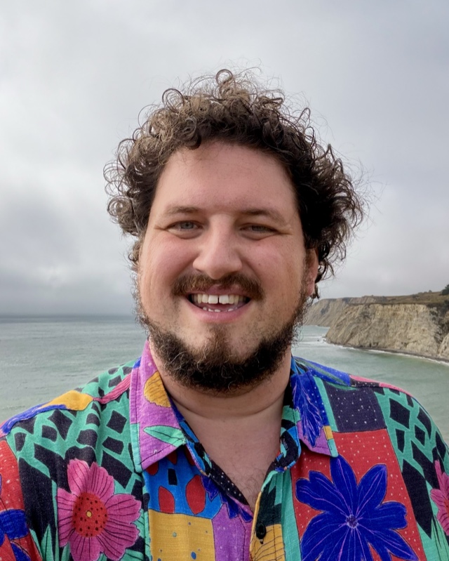 Patrick Angle, smiling, in a collage-print shirt on a cliff above the Northern California coast.